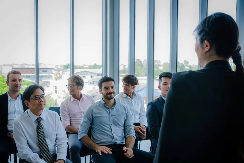 Formadora a apresentar sessão de formação profissional a adultos em sala moderna com participantes atentos e ambiente corporativo.