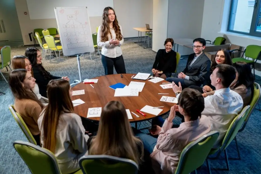 Sessão de formação em grupo com formadora a orientar participantes numa dinâmica de trabalho colaborativo em sala de formação.